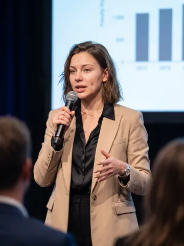 AI influencer Nora giving a keynote on stage with a microphone