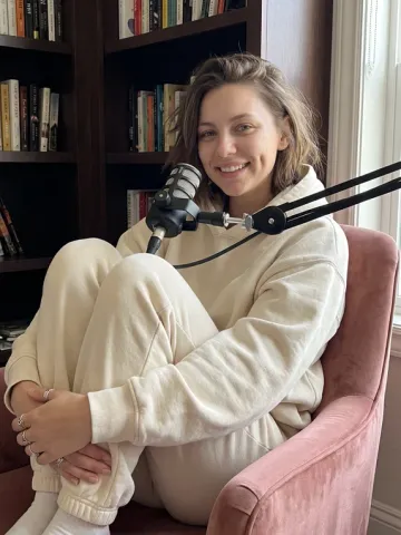 Nora in a cosy podcast studio, sitting by a microphone