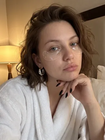 Nora in a white bathrobe with under-eye patches, self-care photo